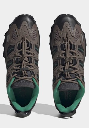 Een paar bruine en zwarte trailrunning schoenen met groene binnenvoering en dikke, robuuste zolen, gezien van boven.