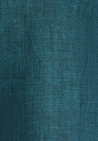 Gros plan d'un tissu tissé vert sarcelle foncé montrant une texture détaillée et un motif de fil entrelacé.