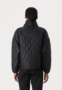 Czarna pikowana kurtka z wysokim kołnierzem, luźnym krojem i fakturowanym wzorem, z gładkim, jednolitym tyłem i elastycznymi mankietami.