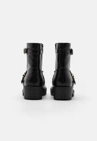 Botines negros de cuero brillante; cuentan con dos correas ajustables, un tacón bajo y una suela texturizada para mayor agarre.