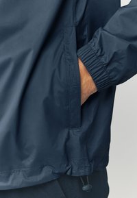 Ľahká námornícka modrá bunda s hladkou textúrou, elastickými manžetami a bočným vreckom. Obsahuje šnúrku na spodnom leme pre nastaviteľné prispôsobenie.