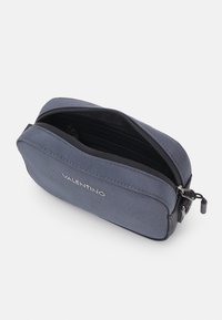 Blue fabric cosmetic bag with a smooth texture, featuring a zip closure and embossed logo on the front. Dimensions are compact and rectangular.