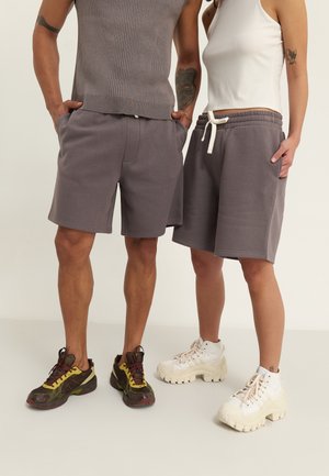 Grijze sportshorts met een elastische tailleband en trekkoord; gladde stof, met zakken. Draagt met contrasterende sneakers.