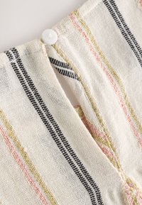 Close-up of cream fabric with pink, yellow, and black stripes, showing a white button fastening a small slit in the material.