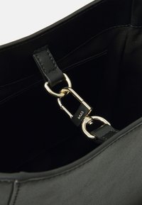 Intérieur d'un sac à main en cuir noir avec des accessoires en or, présentant un attachement par clip et une texture lisse. Design simple et épuré sans motifs.
