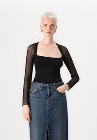 Schwarzer Langarm-Bodysuit mit einem quadratischen Ausschnitt und transparenten Ärmeln, kombiniert mit einem hochgeschnittenen Denim-Rock mit einem Schlitz vorne.