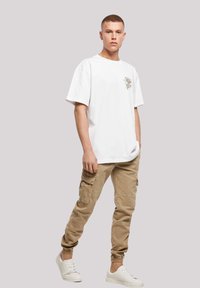Hvid bomulds T-shirt med korte ærmer og et lille farverigt grafisk motiv på brystet, parret med beige cargo-bukser og hvide sneakers.
