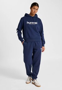 Marinblå hoodie och jogging-set i mjukt material med frontlogotyp, huva med dragsko och elastiska muddar. Texturerad yta, avslappnad passform.