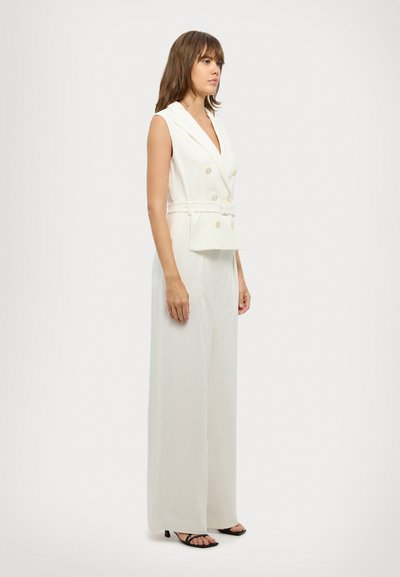 Jumpsuit bianco senza maniche con design doppiopetto, vita cintata e pantaloni a gamba larga. Tessuto liscio e dettagli con bottoni dorati.