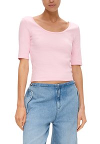 Różowy krótki T-shirt z elastycznego materiału, z okrągłym dekoltem i rękawami do łokcia, zestawiony z jasnoniebieskimi dżinsami.