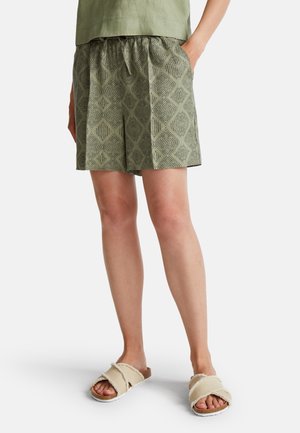 Grüne gemusterte Shorts mit elastischem Bund und seitlichen Taschen, kombiniert mit beigen Riemchensandalen aus weichem Material und Korksohle.
