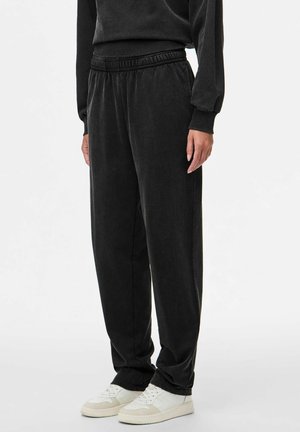Pantalones de chándal negros hechos de tela suave, con una cinturilla elástica y un corte relajado, combinados con zapatillas blancas.
