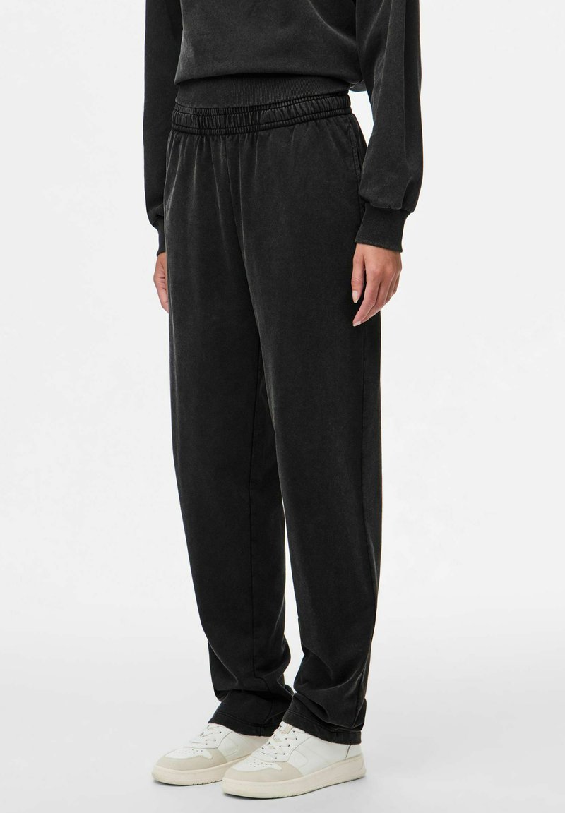 Svarta joggerbyxor i mjukt tyg, med elastisk midja och avslappnad passform, tillsammans med vita sneakers.