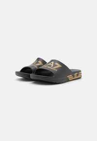 Black slide sandals made from rubber, featuring a glossy finish. Gold logo and accent details on straps with a textured sole.