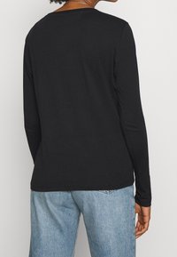 Svart långärmad skjorta med rund halsringning och en slät textur, i kombination med blå denimjeans. Bakifrån visas en enkel design.