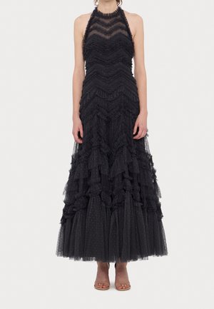 Mujer con un vestido negro sin mangas de capas con patrones de chevron con volantes y tela transparente con puntos, combinado con tacones abiertos nude.