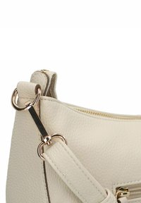 Bolso de cuero color crema con acabado texturizado, que presenta herrajes dorados y cierre de cremallera. La correa es ajustable y tiene acentos metálicos.