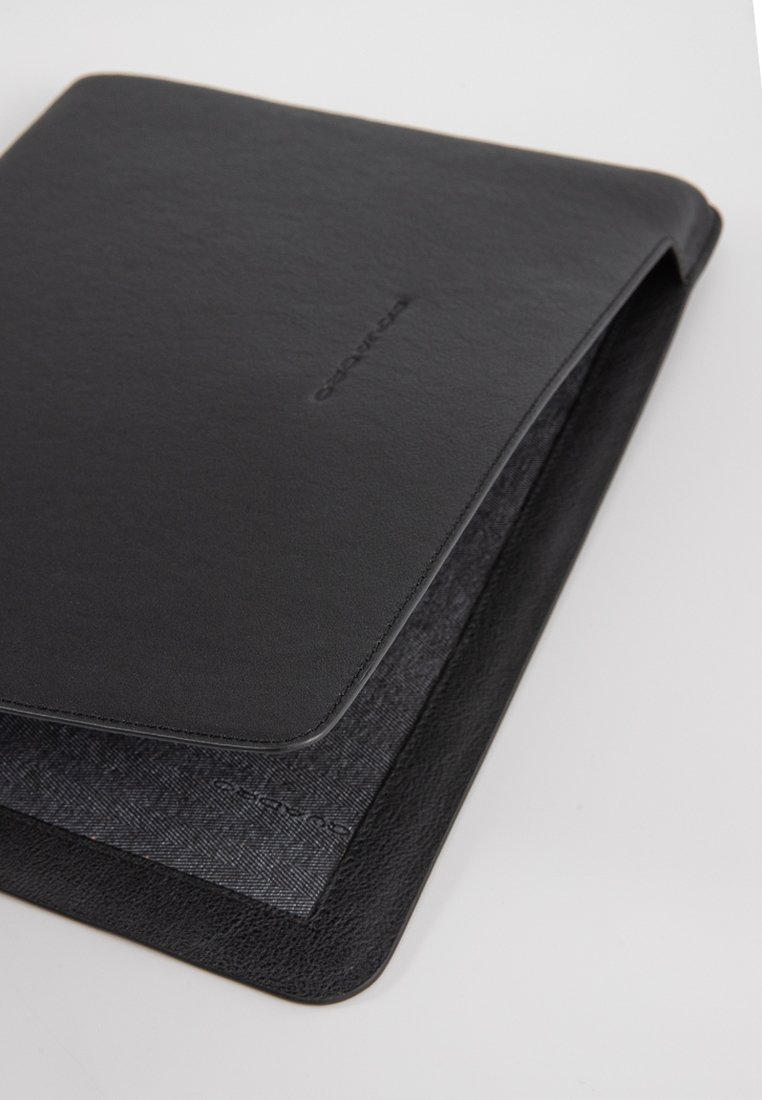 Schwarze Laptophülle aus Leder mit strukturiertem Oberflächen, glatten Kanten und einem kontrastierenden Innenfutter aus Stoff. Dezentes Logo auf der Vorderseite geprägt.