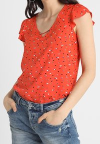 Rode korte mouwen blouse met een V-hals, versierd met een klein hartjespatroon in verschillende kleuren. Gemaakt van lichte stof, met een iets getailleerd ontwerp.