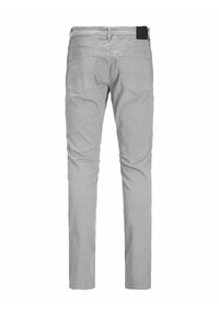 Světle šedé slim-fit džíny zobrazené zezadu se dvěma zadními kapsami a černou nášivkou na pase.