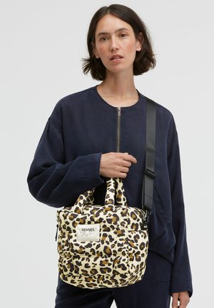 Leopard print handbag with padded texture, cream and brown colors, dual top handles, and a detachable black strap. Embellished with a logo patch.