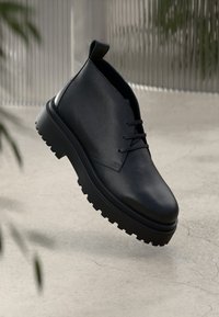 Μαύρες δερμάτινες μπότες μέχρι τις αστραγάλους με υφή, με στρογγυλή μύτη, άνοιγμα με κορδόνια και χοντρή, ανθεκτική καουτσούκ σόλα.