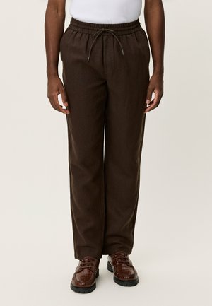 Braune, locker sitzende Hosen aus weichem Stoff mit elastischem Bund und Kordelzug. Kombiniert mit dunklen, strukturierten Schuhen.