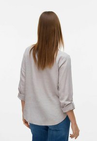 Chemise à manches courtes, de couleur gris clair, fabriquée en lin. Présente des poignets roulés et un ourlet arrondi, conçue avec une texture lisse.