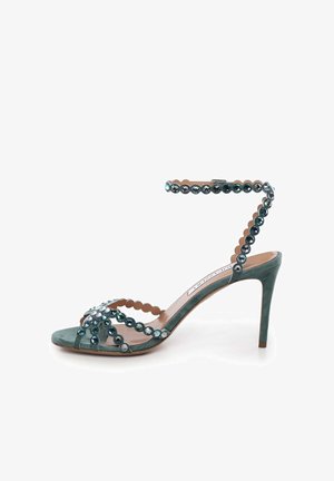 Sandale en daim sarcelle avec un haut talon aiguilles, bordure festonnée et ornée de cristaux ronds le long des lanières et de la cheville.