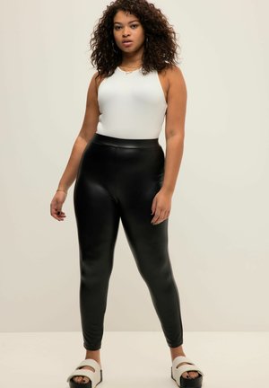 Zwarte faux leren legging gecombineerd met een witte mouwloze top. De legging heeft een glanzende afwerking en een aansluitende silhout.