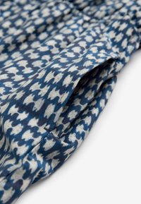 Tissu à motifs bleu et blanc avec un petit détail de poche, montrant des coutures et de légers fronces dans le tissu.