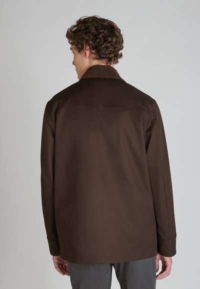 Chaqueta marrón con cuello, de textura suave, que presenta un corte recto y mangas largas. Costuras visibles y un diseño de ajuste relajado.