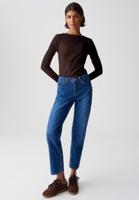 Braun gerippter Langarmoberteil mit Boot-Ausschnitt, kombiniert mit blauen geraden Denim-Jeans und braunen Schnürsneakern.