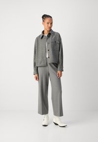 Gray checkered jacket with a cropped design, single chest pocket, and button closure, paired with wide-leg gray trousers and white boots.