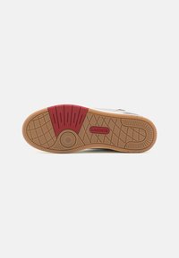 De buitenzool van de Lacoste sneakers heeft een basis van gumrubber met een rood en textuurpatroon voor grip. Cirkelvormig logo-detail is inbegrepen.