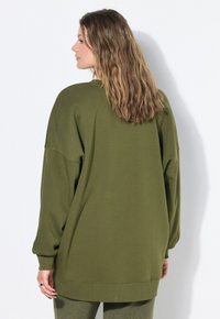 Sweatshirt oversize vert olive avec des manches longues, un col rond et une coupe décontractée. Texture douce et poignets côtelés. Design à dos sans couture.