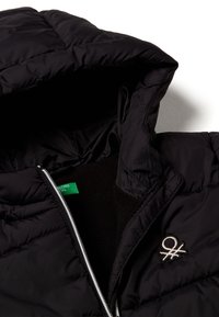 Giacca nera imbottita con chiusura a zip, dotata di un interno morbido, un'etichetta verde e un piccolo logo ricamato sul petto.