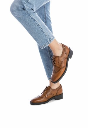 Zapatos de vestir de cuero marrón con detalles de brogue, diseño de cordones, suela plana de goma negra, combinados con jeans claros azules con dobladillo.