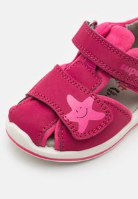 Vaaleanpunaiset lasten sandaalit, joissa on tarranauha, tähtimuotoinen koriste, avotossu-mallinen design ja valkoinen kumipohja. Pehmeää mokkaa.