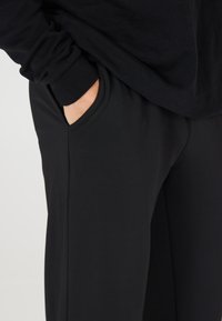 Sorte sweatpants i bomuldsblanding med afslappet pasform, sidelommer og en glat overflade, parret med en matchende sort langærmet top.
