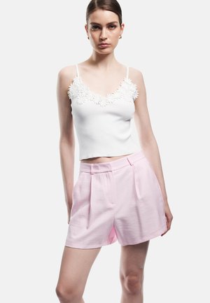 Witte mouwloze top met gestructureerde bloemversieringen bij de halslijn, gecombineerd met lichtroze high-waisted shorts met plooien.