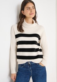 Cremfarbener Rollkragenpullover mit horizontalen schwarzen Streifen, weicher Textur, gerippten Bündchen, kombiniert mit blauen Jeans. Minimalistisches Design, lässiger Look.