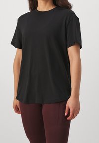 Czarny t-shirt z krótkim rękawem o luźnym kroju, okrągłym dekolcie i gładkiej fakturze, zestawiony z bordowymi legginsami z detalami na suwak.