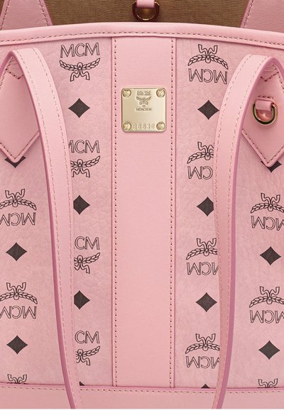 Zaino MCM in pelle rosa con motivi ripetuti del logo nero, piastra centrale dorata del brand e spallacci regolabili visibili.