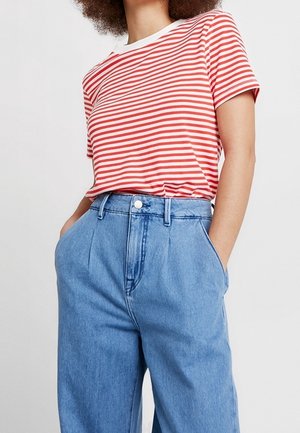Personne portant un t-shirt à manches courtes rayé rouge et blanc, rentré dans un jean bleu ample taille haute, les mains dans les poches.