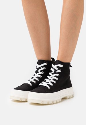 Schwarze High-Top-Canvas-Sneaker mit weißen Schnürsenkeln, strukturiertem Obermaterial und einer auffälligen, klobigen weißen Sohle, die hinten eine Zuglasche hat.