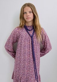 Vestido morado de manga larga con un patrón de estampado de leopardo. La tela es suave, con un escote alto y un dobladillo de volantes en capas. Accesorios con un collar de cuentas morado.
