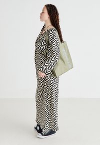 Robe longue noire et blanche à motifs avec un design géométrique, associée à un sac fourre-tout vert et des baskets noires. Tissu lisse, coupe pleine longueur.