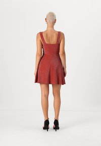 Robe pailletée rouge avec une jupe évasée, un décolleté carré et de larges bretelles. Associée à des sandales à talons hauts noires.