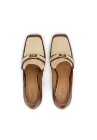 Chaussures plates en cuir beige et marron avec des orteils carrés, ornées d'une boucle en or et d'une texture lisse. Logo de la marque sur la semelle intérieure.